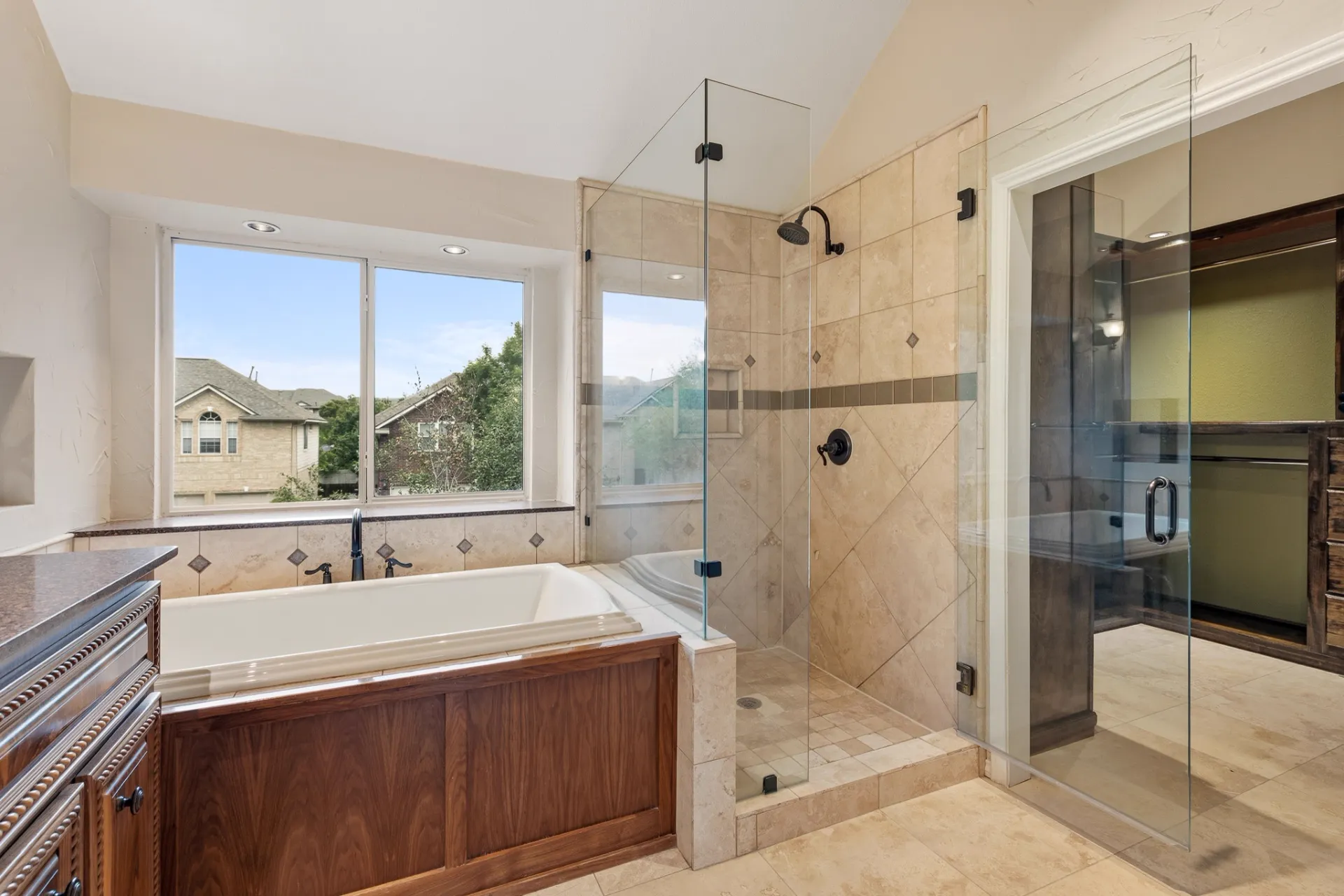 Primary bath soaking tub and frameless walk-in shower with travertine tile
