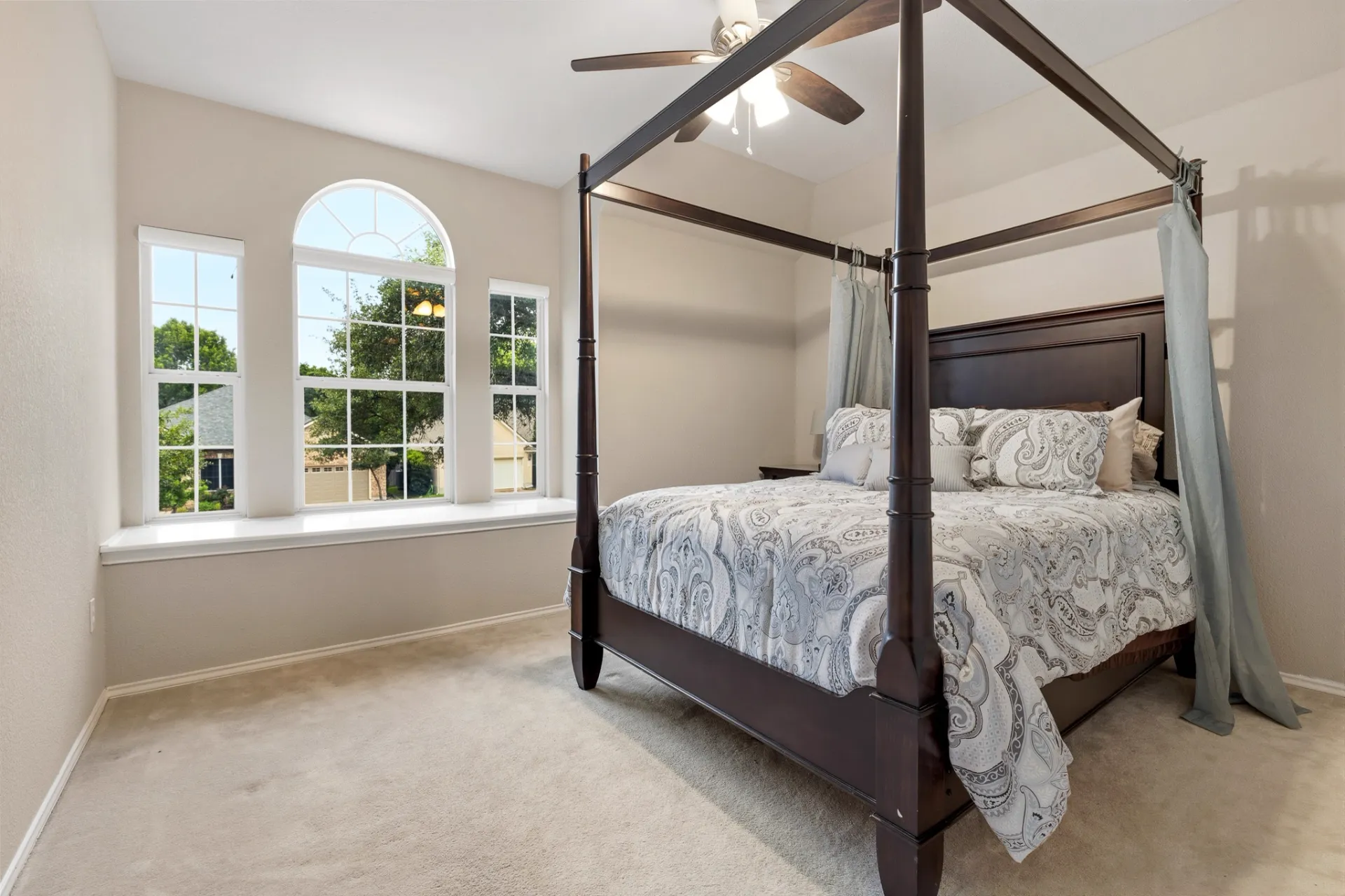 Guest bedroom with arched window, four-poster bed, and tree views