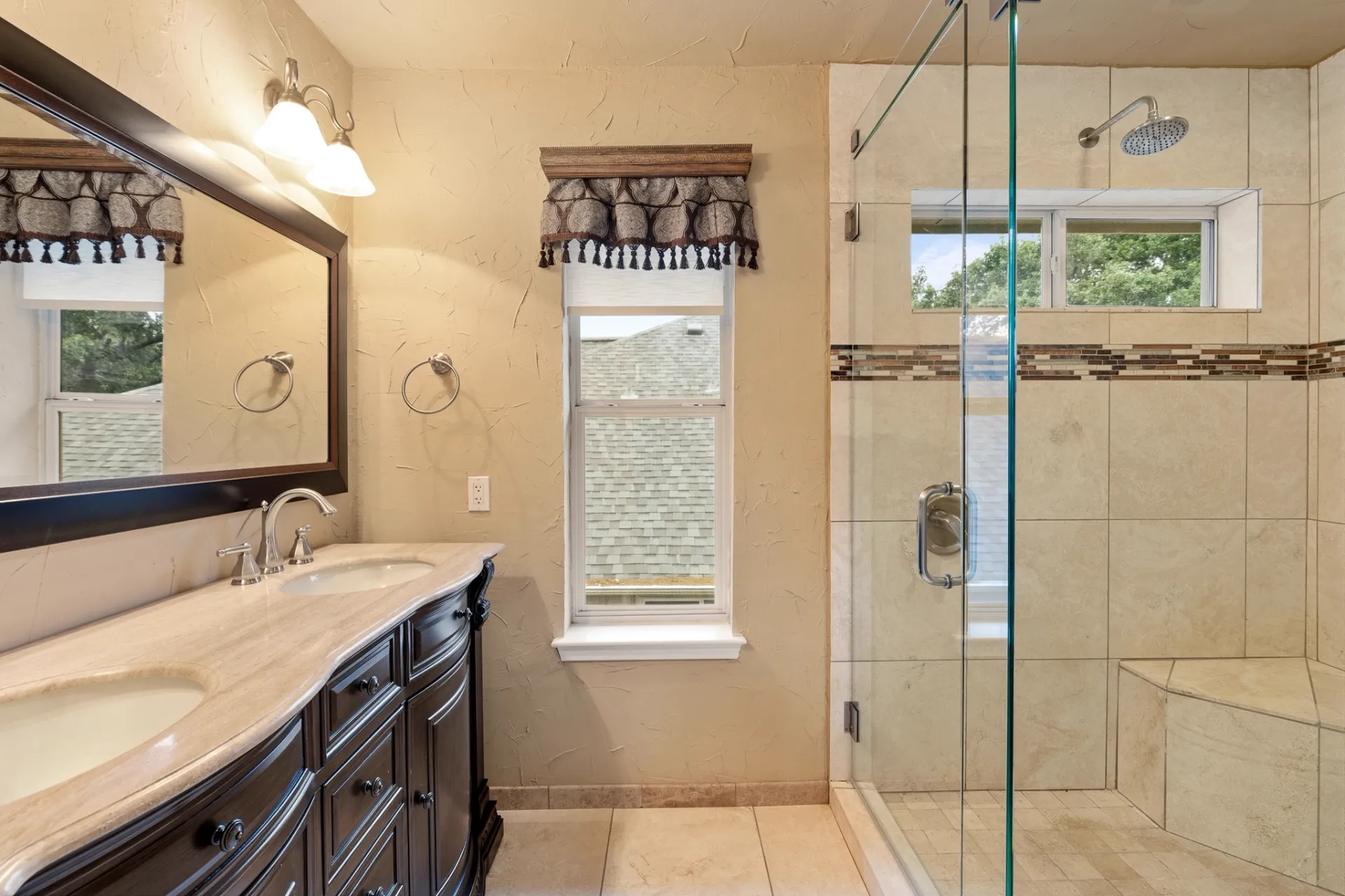 Full hall bathroom with travertine shower and dual-sink vanity